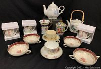 Full lot overview showing various teapots, mugs, and teacups arranged on black background.