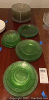 Photo showing stacks of green uranium glass plates and clear plates in stacks on a wooden surface, with one clear ornate bowl.