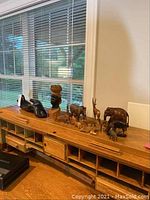 Wide view of all African animal figurines and sculptures displayed on wooden desk under window with blinds