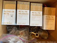 Boxes of West Elm metal pin holdbacks and other curtain hardware including rings and brackets, showing item labels and packaging.