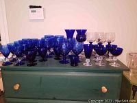 Overview showing various cobalt blue glasses grouped on a green chest, featuring different shapes and sizes.