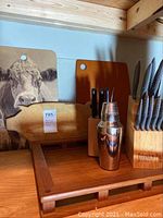 Wooden tray, wooden cutting boards, knife blocks with knives, and cocktail shaker displayed on tray