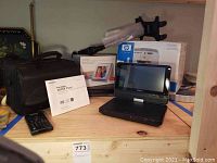 Lot items displayed on wooden surface including Sony portable CD DVD players, Brookstone digital photo album, HP Photosmart 325 printer, Sony DVD player with accessories and carrying case.