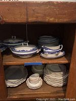 Photo showing 3 covered casserole dishes, stacked plates and a gravy boat inside a cabinet shelf.