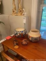 Two ethnically styled ceramic bowls, one small incense burner, and a carved wooden totem pole figurine on a wooden table near a window.