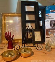 Group photo showing gold ornate frame, black multi-photo frame, red hand sculpture, photo frame easel, and gold candle holders on table.