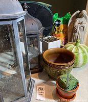 Lot contents including two metal hexagonal hurricanes, ceramic planters, angel statue, pumpkin container with soil, and a bag of potting soil mix