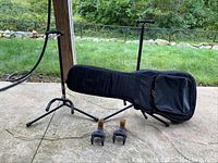Wide shot showing 2 black adjustable FretRest guitar stands and black Access guitar bag with backpack straps resting on one stand.