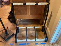 Front view of the Konig & Meyer guitar stand showing 3 double slots with white protective holders on the metal frame, standing on a wooden floor with some scratches visible on the frame.