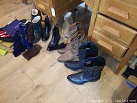View of leather boots in various styles and colors, leather gloves, and bags placed on wooden floor near furniture.