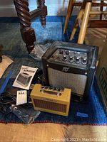 Two Fender mini guitar amplifiers on the floor, one yellow vintage style Mini Twin-Amp and one black Mustang Mini, with power cords and Fender manual beside them.