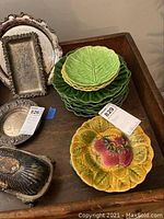 Photos of various plates including majolica leaf-shaped salad plates and silver-tone serving trays on a wooden surface.