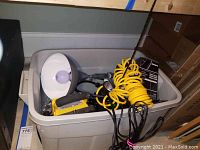 Portable flood lights with large bulbs and attached cords, yellow coiled hose, black cords inside a large gray plastic bin.