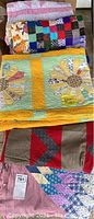 Four vintage quilts stacked, showing a sunflower appliqué quilt with yellow and green tones and other colorful patchwork quilts underneath