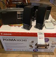 Lot items shown on top of Canon PIXMA MX340 printer box. Items include Sony AM/FM radio, Insignia radio with HD Radio/iPod dock and speakers, and a small white device (possibly a microphone or remote).