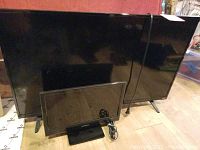 Two televisions placed one in front of another on a floor, showing size difference and physical condition.