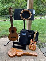 Full lot shot showing ukulele, guitar stand, music stand with tambourine, 2 Pedaltrain cases, guitar-shaped clock, and decorative carved guitar-like item