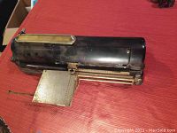 Front angle showing the entire black metal check writer with paper holder extended.