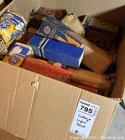 Top view of cardboard box filled with various vintage lightbulb boxes, some labeled General Electric and others in plain blue boxes.