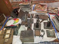 Photo showing a variety of vintage electrical and scientific parts including wood and metal bases, glass lenses with chips, color wheels, and a stack of magazines in the background.