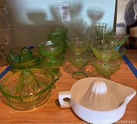 Photo showing multiple green uranium glass juicers, bowls, and goblets, and one white milk glass Sunkist juicer.