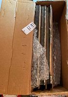 Top-down view into cardboard box showing six stacked leaded beveled glass window panels wrapped with bubble wrap