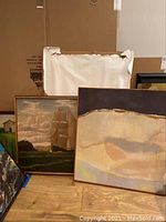 Two framed paintings on floor against a wall. One shows a sailing ship, the other an abstract design