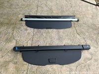 Two cargo covers laid on the ground: one is black with silver side rails, the other is fully black with a handle in the middle.