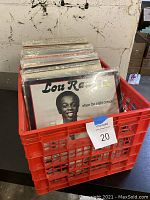 Red plastic milk crate filled with over 85 vinyl records, Lou Rawls album 'When the Night Comes' visible at front, showing protective plastic sleeves on many records.