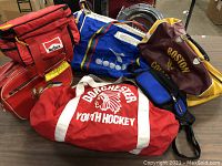 Photo showing six assorted vintage bags on a table including the Marlboro cooler bag, Diadora duffel bag, Dorchester Youth Hockey duffel, Boston College handbag, blue fanny pack and the 1960s printed handbag.