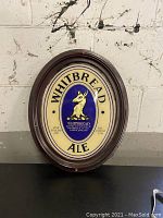 Whitbread Ale oval gilded sign with dark wood frame, cream background and central blue and gold graphic with dog illustration