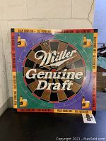 Front view of a Miller Genuine Draft metal sign with a dartboard design featuring four images of beer bottles, the Miller Genuine Draft logo in the center.