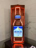Photograph of Busch Beer neon sign powered on showing orange neon lit outline and lit graphic panels.