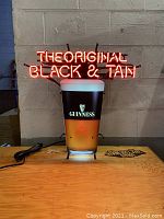 Lit neon sign showing "THE ORIGINAL BLACK & TAN" in red neon over a Guinness pint with Bass logo.