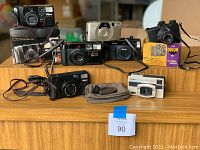 Lot of eight 35mm film cameras arranged on wooden steps, showing various models and brands including Nikon, Pentax, Canon, Argus and Orion, all used and untested.