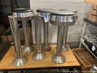 Set of six metal diner style stool bases with four black cushioned seats arranged on top. The metal has visible rust and wear, the black seats show fading and marks.