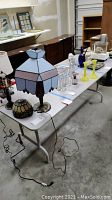 White folding table shown with various decorative items displayed on top in warehouse setting.