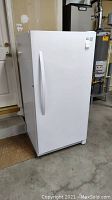 Front and left side view of white upright freezer on concrete floor
