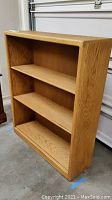 Full angled view of the oak plywood bookcase showing three adjustable shelves and wood grain detail.
