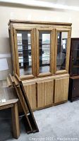 Full view of oak display cabinet showing three glass front doors on upper section and wooden lower cabinet doors with a drawer.
