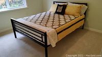 Queen size bed fully assembled, showing metal frame and wooden accent headboard and footboard with bedding on mattress.