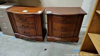 Pair of dark brown wooden side tables with three drawers each and curved fronts.