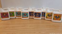 Photo of 10 different 1L nutrient solution bottles on a wooden floor showing front labels and caps.