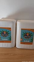 Photo of two white plastic nutrient containers labeled Ganja Grow Part A and Part B with nutrient ratios 5-0-2 and 1-5-8 respectively.