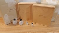 Four frosted white Alfred Sung Pure perfume bottles of varying sizes alongside two wooden gift boxes and matching paper bags, all brand labeled.