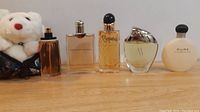 Full view of five perfume bottles and Nicole Miller plush bear bag on a wooden surface