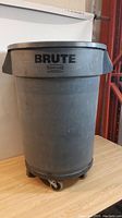 Large gray Brute garbage can on rolling dolly, side view showing overall shape and caster wheels.