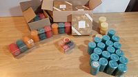 Lot of various boxed and packaged candles on wooden surface, displaying different brands and colors.