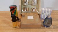 Photo of Alfred Sung candle set, Bob Mackie perfume bottle and box, and Lulu Guinness perfume bottle and box on wooden surface.