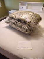 Queen size bedding set items wrapped in plastic on a bed, showing paisley print comforter and pillow shams.